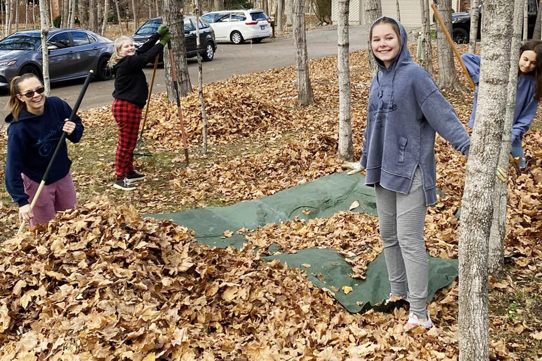4 girls serving by raking fall leaves. Each is bundled against the cold and holding a rake