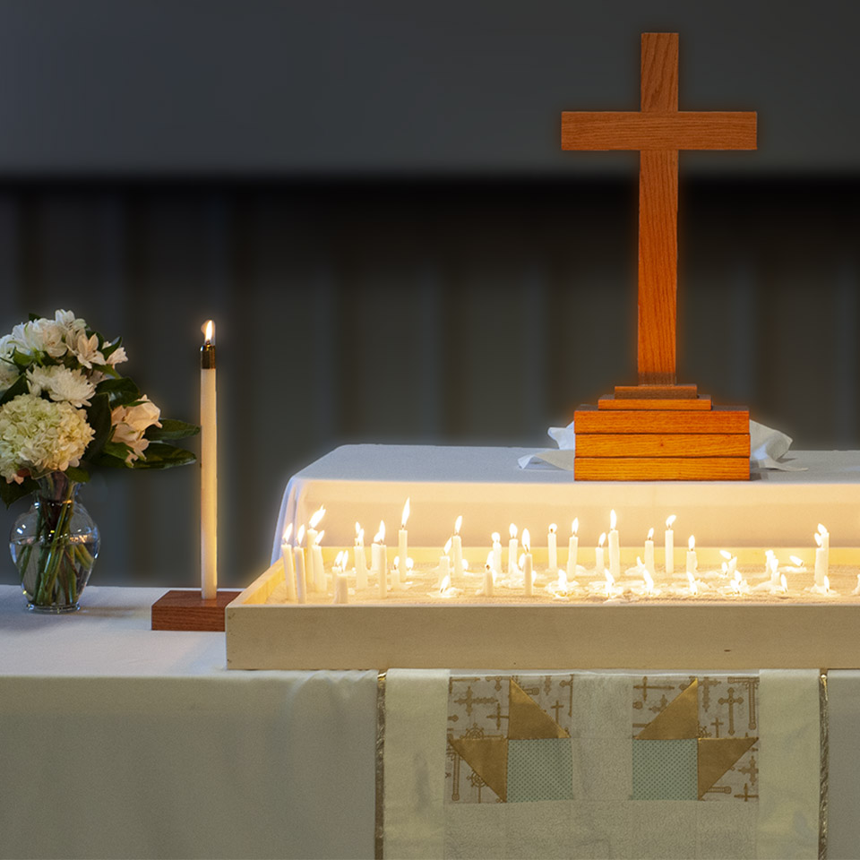 Cross of Jesus on an altar surrounded by flowers and the soft glow of dozens of lit candles