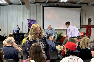 Congregation of Faith Lutheran Church of McLean County gathering in chairs to worship. A cross and video screen are in the background