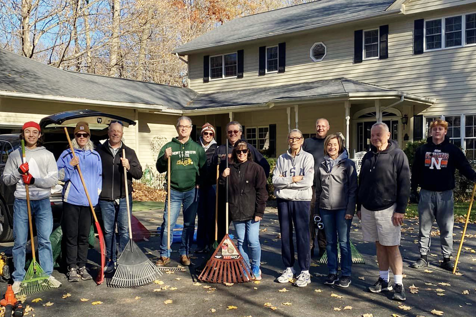 A group of youth and adults from Faith Lutheran Church of McLean County stand with rakes and tools in a driveway in central Illinois