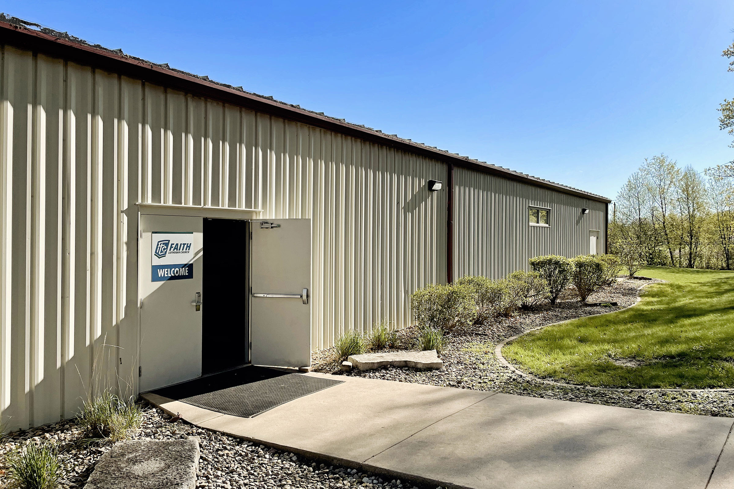 Open door to the building of Faith Lutheran Church of McLean County with blue sky and trees in the background