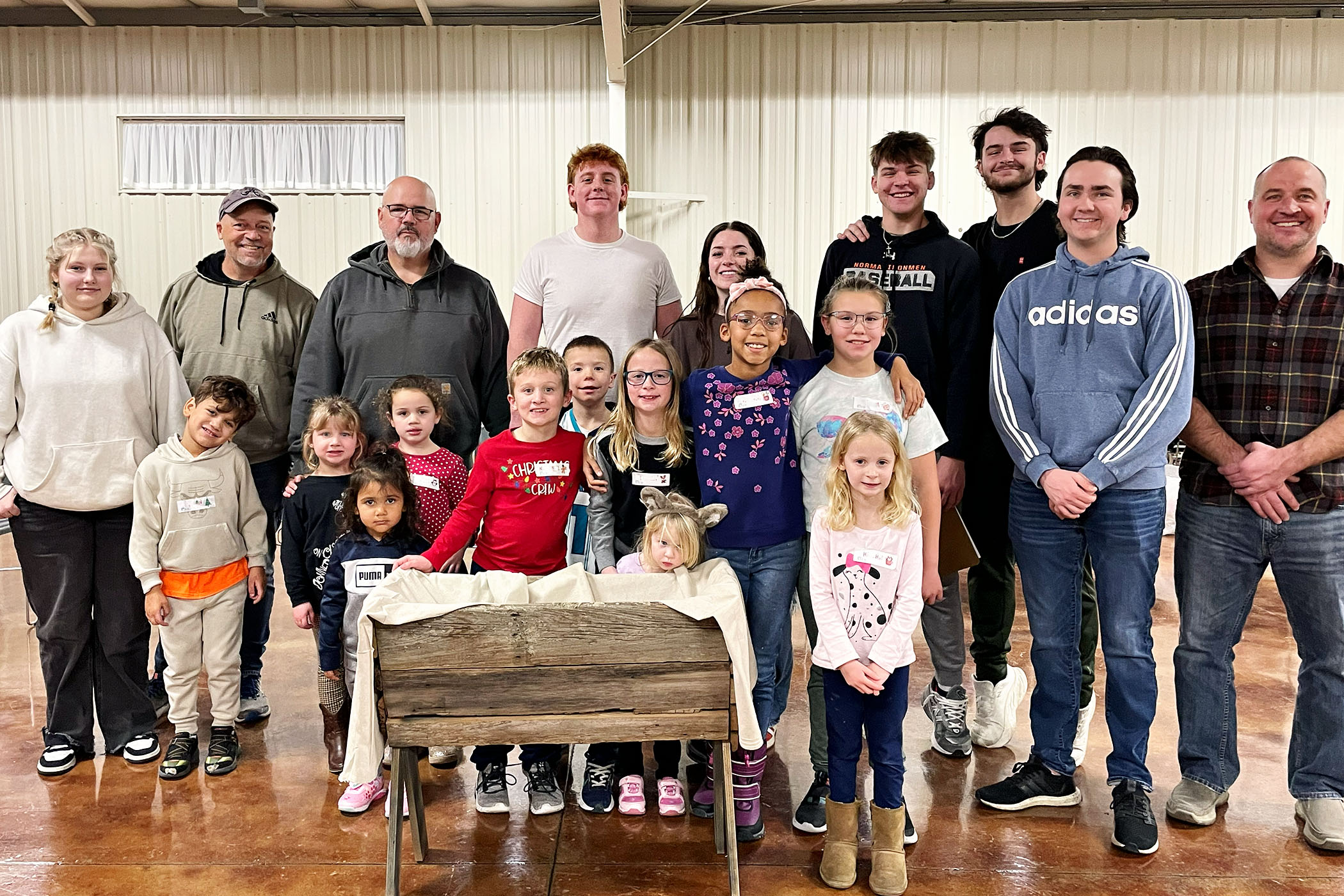 Children and Adults smiling at camera standing near a replica of Baby Jesus' manger during a Pageant Weekend Event at Faith Lutheran Chruch of McLean County in Bloomington Illinois